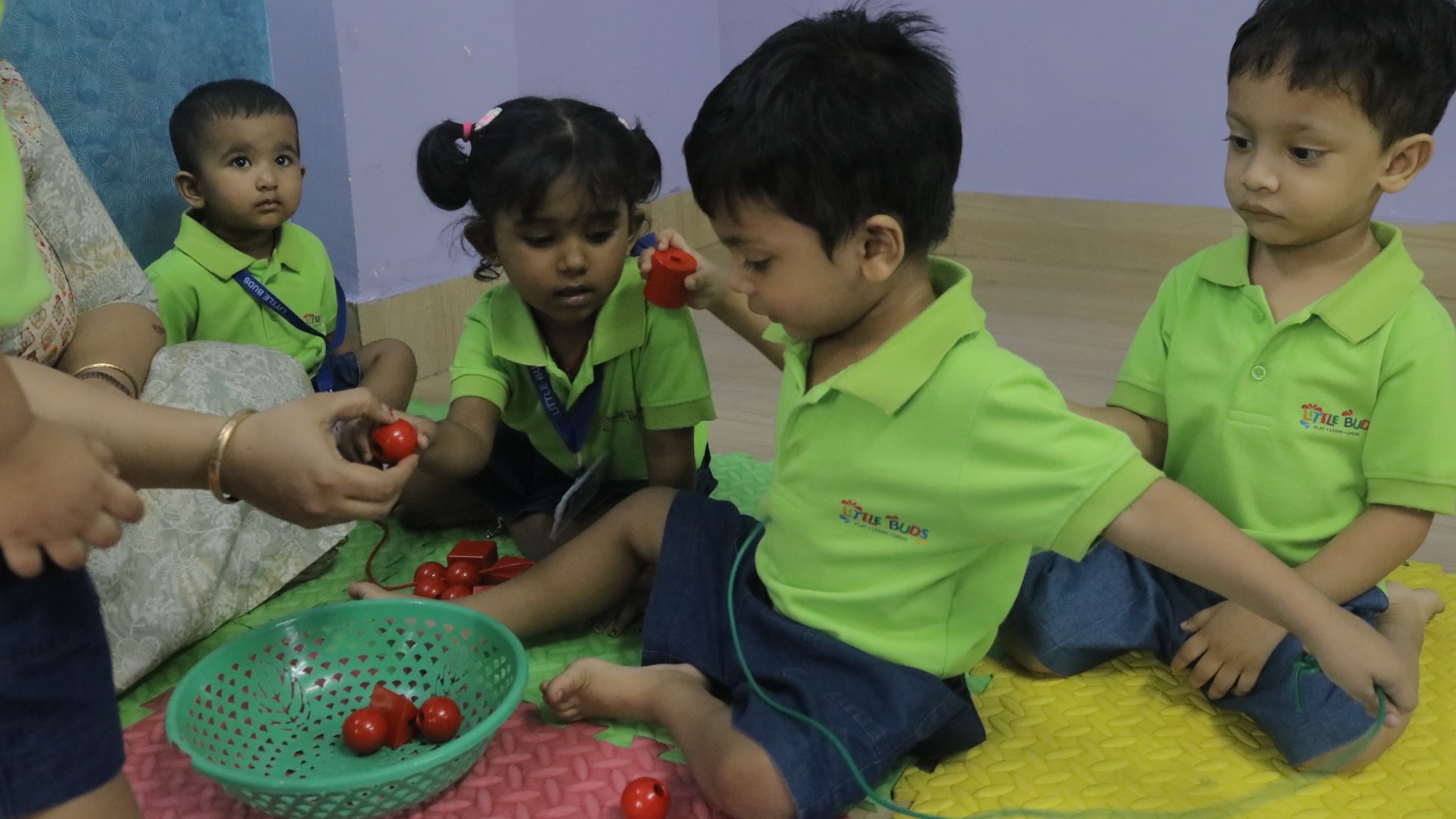 Playgroup children sitting on the play mat with a teacher, exploring beads and toys